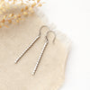 The silver beaded bar earrings styled on tan linen with dried grass