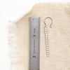 A silver beaded bar earring next to a ruler for size reference