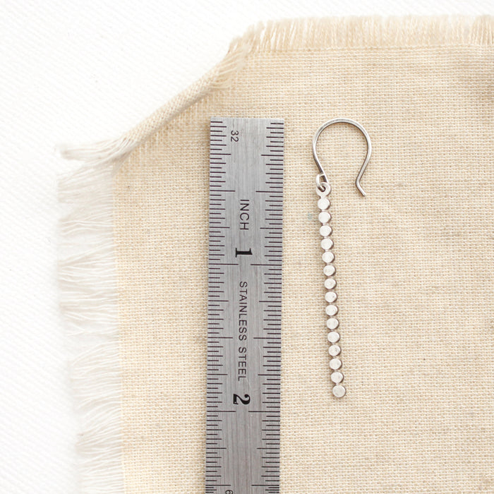 A silver beaded bar earring next to a ruler for size reference