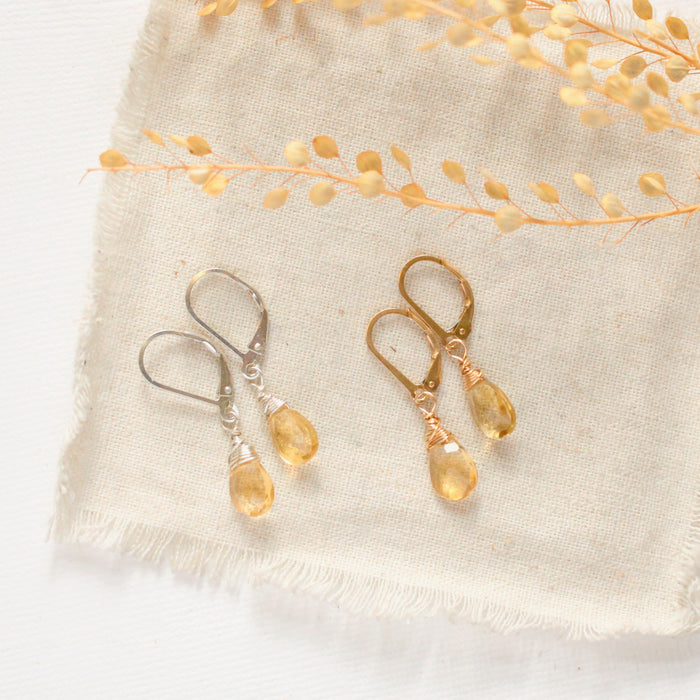 The silver and gold citrine drop earrings styled on tan linen with dried grass