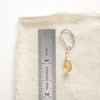 A silver citrine drop earring next to a ruler for size reference