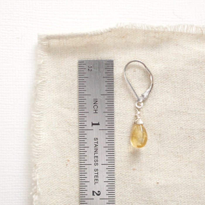 A silver citrine drop earring next to a ruler for size reference