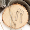 The silver open bar earrings styled on wood with gray velvet and dried grass