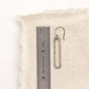 A silver open bar earring next to a ruler for size reference