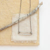 The silver open bar necklace styled on a tan rock with linen and a wooden stick