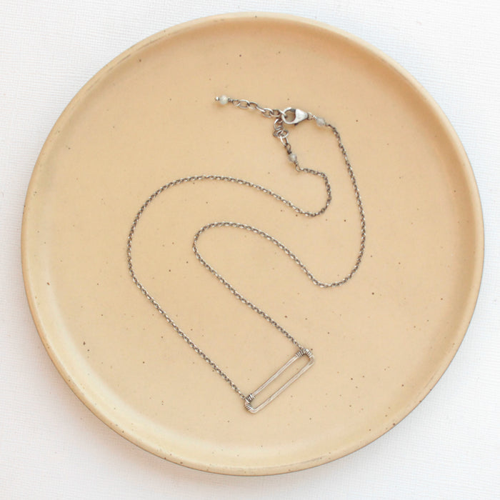 The silver open bar necklace styled on a tan plate to show the adjustable lobster clasp closure