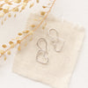 The silver open heart earrings styled on tan linen and dried grass
