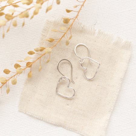 The silver open heart earrings styled on tan linen and dried grass