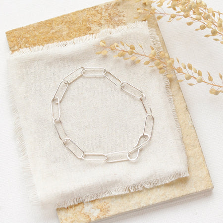 The silver paperclip styled on a tan rock with linen and dried grass