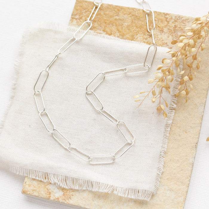 The bright silver paperclip necklace styled on a tan rock with linen and dried grass