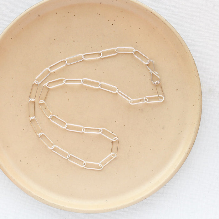 The bright silver paperclip necklace styled on a tan plate to show the whole chain