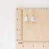 The pinned silver pearl earrings styled on a wooden ruler for size reference