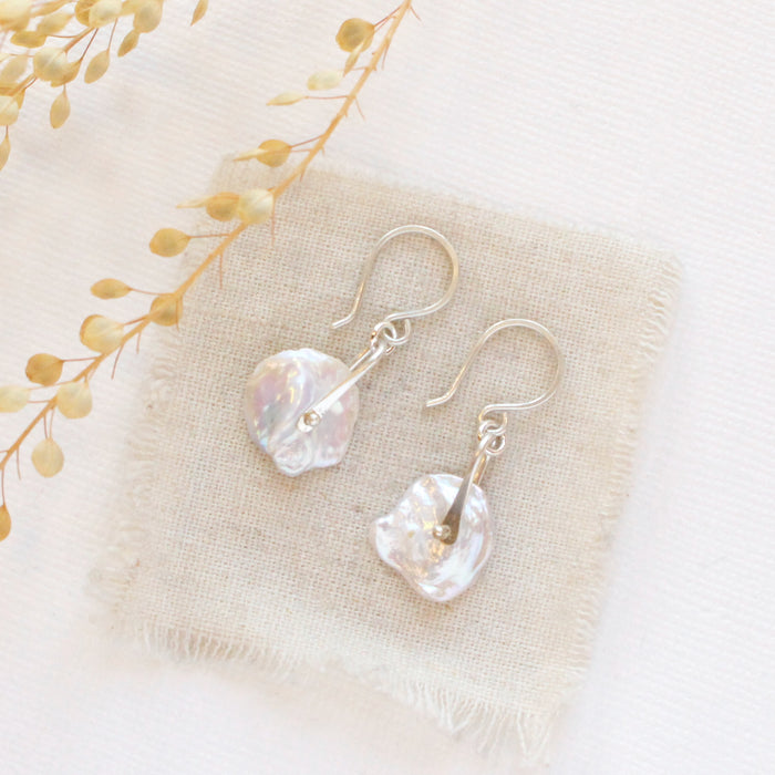 The silver pinned pearl earrings styled on tan linen with dried grass