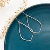 The silver pointed hoop earrings styled on a blue plate with dried grass