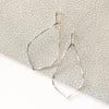 The bright silver pointed hoop earrings styled on gray leather