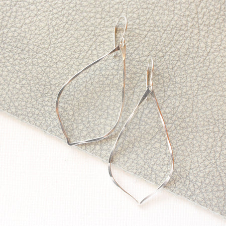 The bright silver pointed hoop earrings styled on gray leather