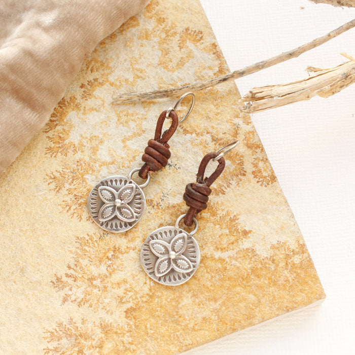 The silver wanderer coin leather earrings styled on a tan rock with velvet and dried grass