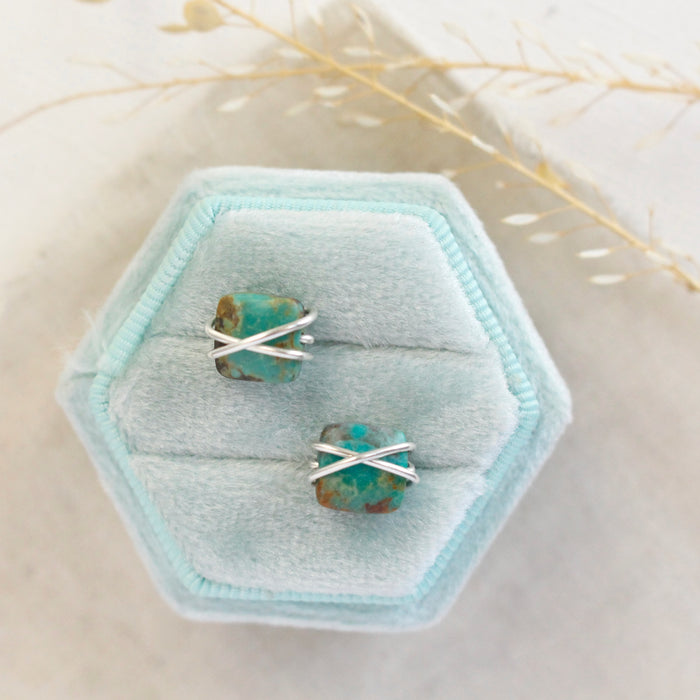 The silver wrapped turquoise square post earrings styled on a blue velvet box with linen and dried grass