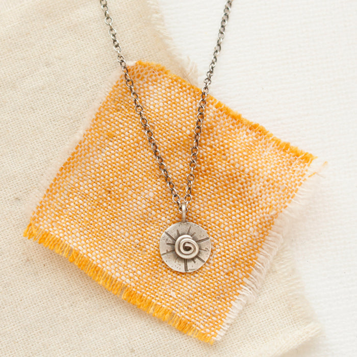 The small musana sun necklace styled on tan and orange linen