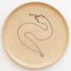 The small musana sun necklace styled on a tan plate to show the adjustable lobster clasp closure