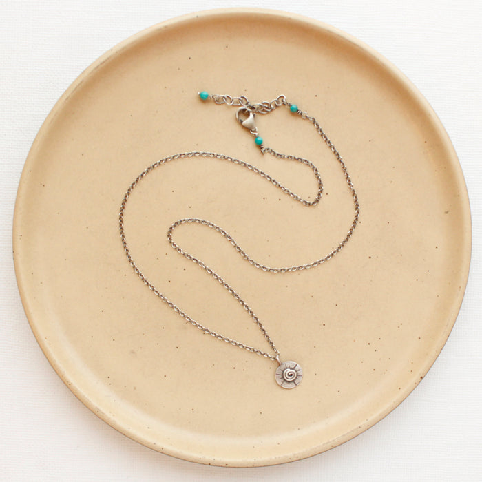 The small musana sun necklace styled on a tan plate to show the adjustable lobster clasp closure