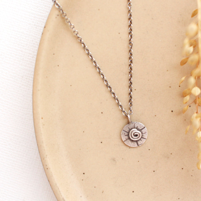 The small musana sun necklace styled on a tan plate with dried grass