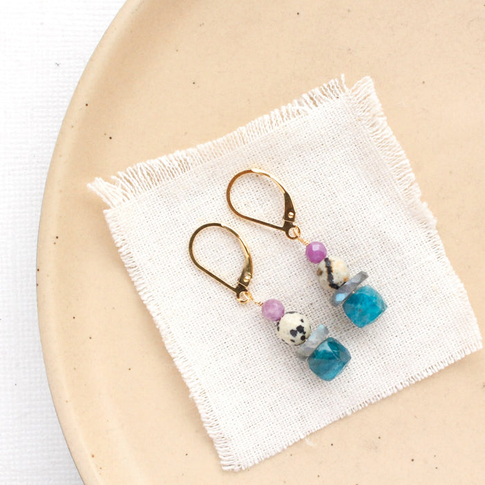 The stacked capri earrings styled on a tan plate with linen