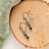 The stacked blue tourmaline earrings styled on wood with green velvet and dried grass