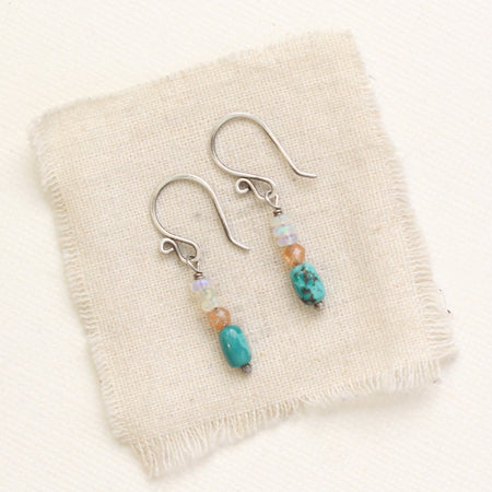 The stacked ethiopian opal, sunstone, and turquoise earrings styled on tan linen