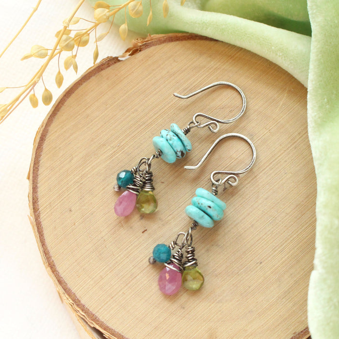 The colorful stacked elise earrings styled on wood with green velvet and dried grass