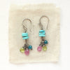 The colorful stacked turquoise, peridot, ruby, and apatite earrings styled on tan linen