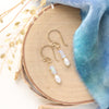 The stacked opal and pearl earrings in gold fill styled on wood with blue velvet and dried grass