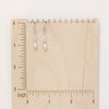 The stacked opal and pearl earrings on a wooden ruler for size reference