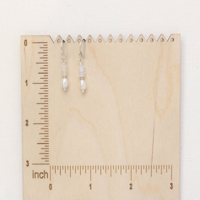 The stacked opal and pearl earrings on a wooden ruler for size reference