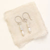 The stacked opal and pearl earrings in silver styled on tan linen