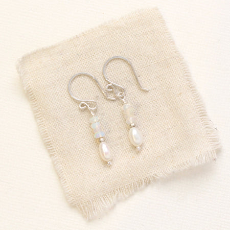 The stacked opal and pearl earrings in silver styled on tan linen