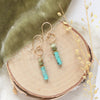 The stacked lana earrings styled on wood with green velvet, wood, and dried grass
