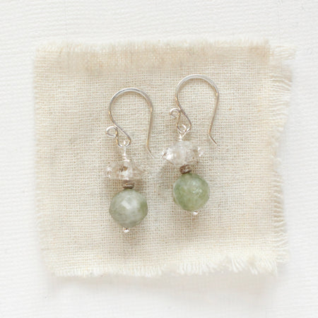 The stacked herkimer diamond and aquamarine earrings styled on tan linen