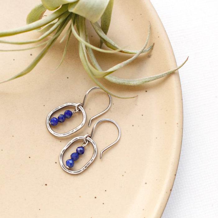 The stacked lapis mini hoop earrings styled on a tan plate with an air plant