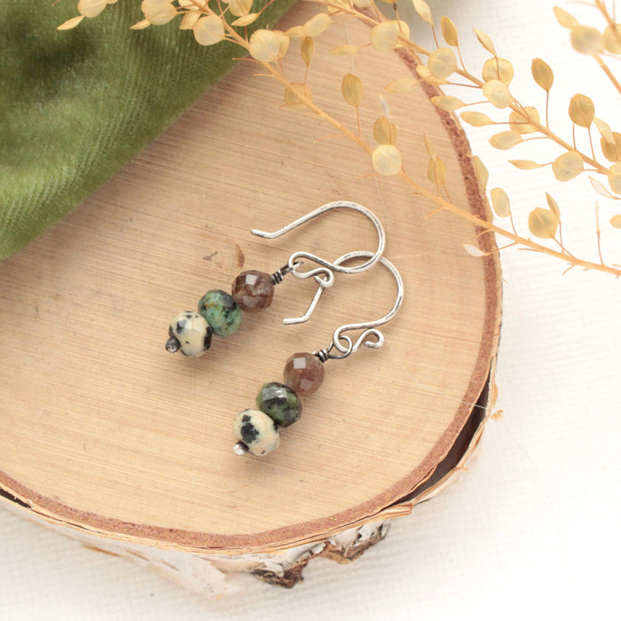 The stacked lona earrings styled on wood with green velvet and dried grass