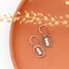 The stacked pearl mini hoop earrings styled on an orange plate with dried grass