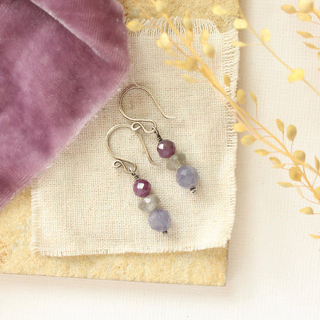 The stacked vinca earrings styled on a tan rock with linen, purple velvet, and dried grass