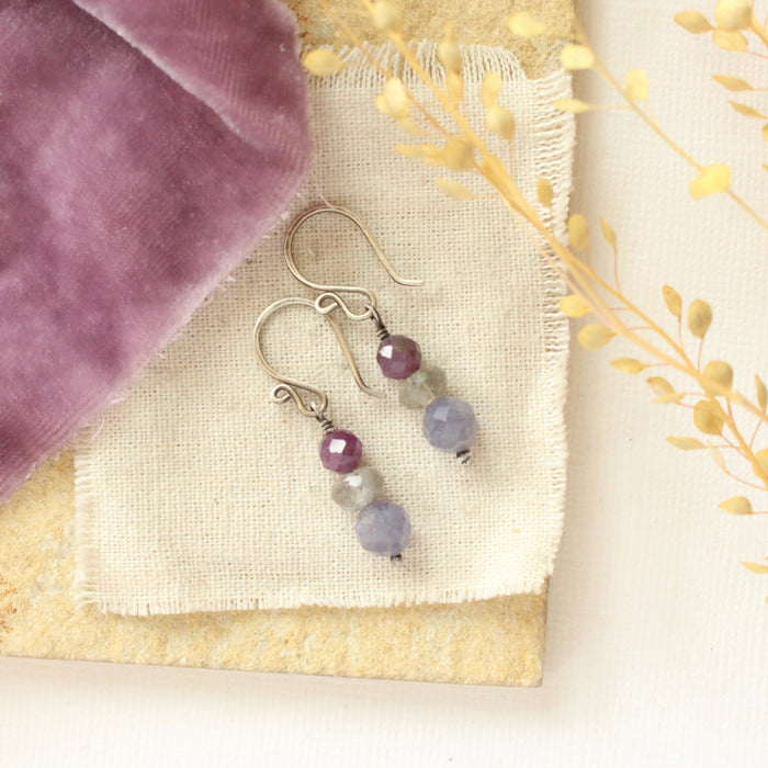 The stacked vinca earrings styled on a tan rock with linen, purple velvet, and dried grass