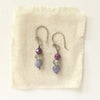 The stacked vinca earrings styled on tan linen
