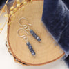 The stacked sapphire earrings styled on wood with blue velvet and dried grass