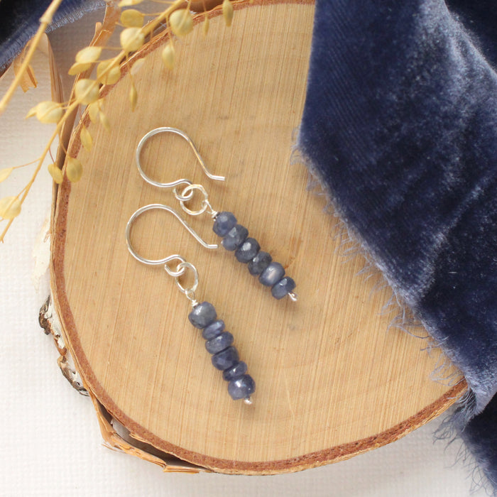 The stacked sapphire earrings styled on wood with blue velvet and dried grass