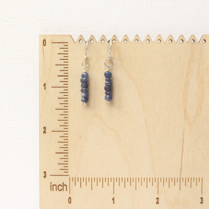 The stacked sapphire earrings on a wooden ruler for size reference