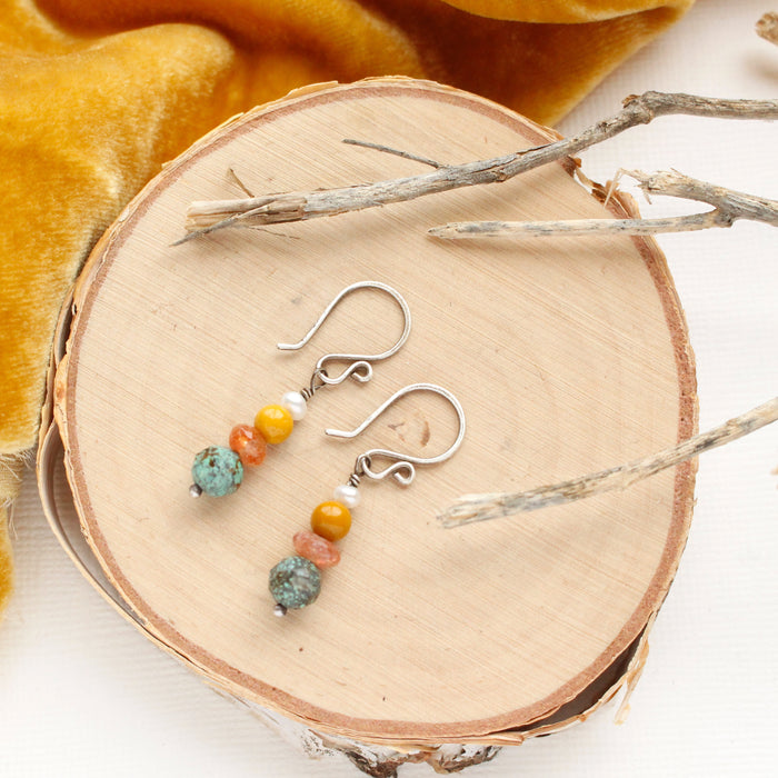 The stacked sunset earrings styled on wood with yellow velvet and dried grass