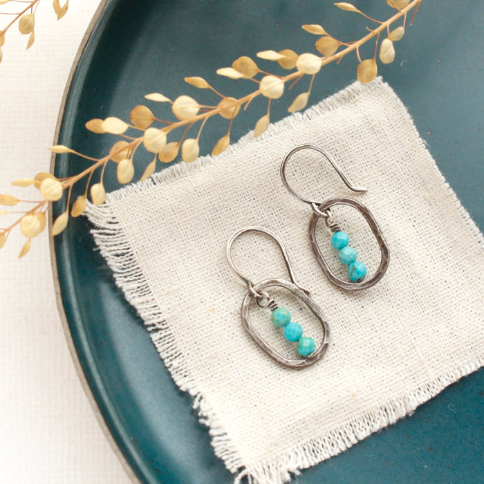 The stacked turquoise mini hoop earrings styled on a blue plate with tan linen and dried grass