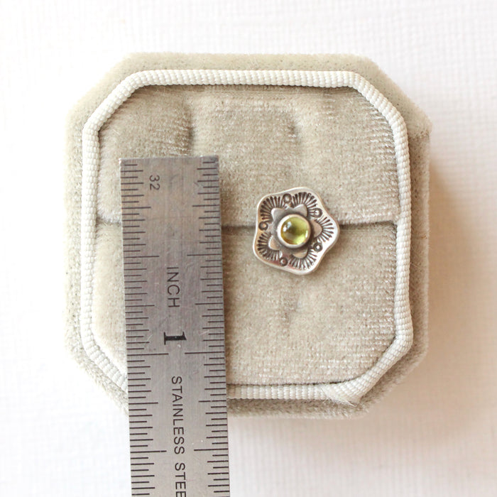 A stamped flower peridot post earring next to a ruler for size reference